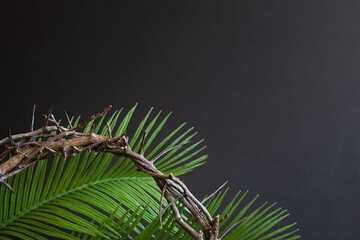 Crown of thorns and palm leaves on a black background with copy space
