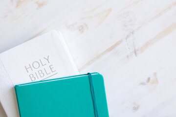 Closed holy Christian bible on a white wood background with a teal journal with copy space