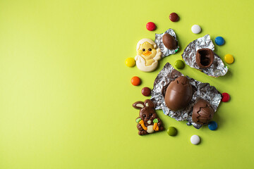 Easter background from chocolate Easter eggs and colorful candies on a green backdrop. Top view and copy space.
