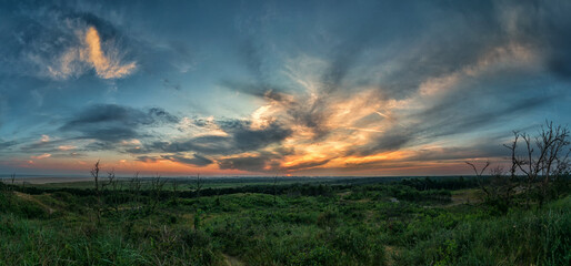 Wide-angle shot of a greenfield with the golden sun setting behind the clouds