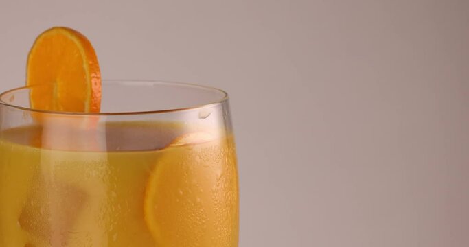 closeup rotating glass fill with orange juice ice cube frost on the glass slice of orange on the rim