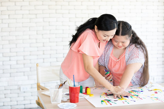 woman teacher and down syndrome girl with painted hands, drawing a picture on paper