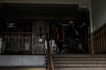 People passing by the stairs inside the old, dark train station.