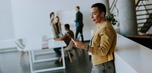 Young short hair business woman standing in office and using digital tablet in front of her team