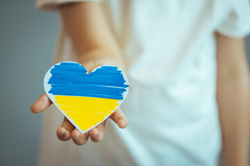Heart with print the national flag of ukraine in child hands. Hand holding a heart made from the flag of Ukraine blue yellow on an isolated gray background.