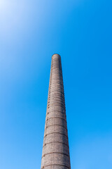 Tall, brick, industrial chimney located in Porcelain Factory (Fabryka Porcelany) in Katowice, Silesia, Poland against blue, cloudless sky.