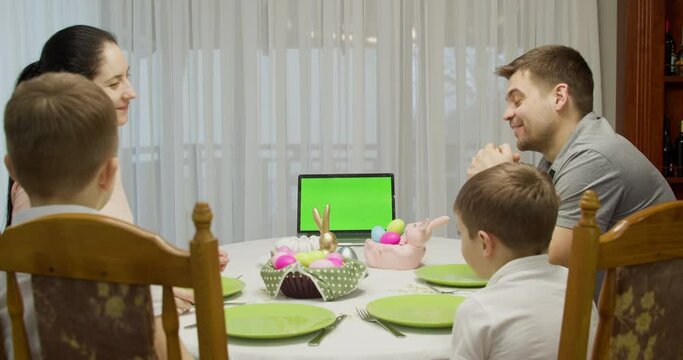 green screen notebook. Parents with two teenage boys talking video call using a laptop, enjoying spending time together on the weekend, at home, at the holiday table prepared for Easter