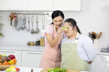 mother cutting fresh peppers on wooden cutting board with down syndrome teenage girl or her daughter in the kitchen