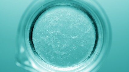 Top view macro shot of glycerin being poured into a beaker with water and dissolves in it on cyan...
