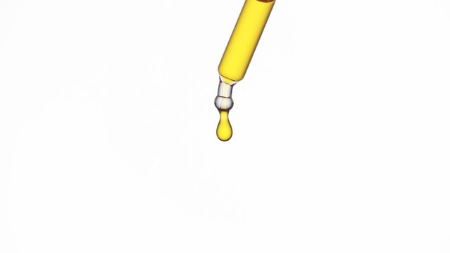 Drop of yellow transparent liquid is hanging from lab dropper on white background | Abstract face care lotion ingredients mixing concept