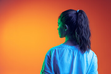 Back view portrait of young girl with ponytail in white T-shirt posing isolated over gradient...
