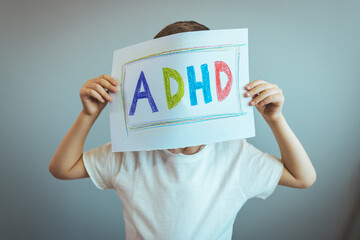 Young boy holds ADHD text written on sheet of paper. ADHD is Attention deficit hyperactivity disorder. Close up. Boy holding paper and admitting suffering from ADHD. - obrazy, fototapety, plakaty