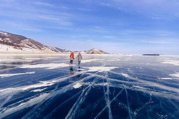 Two young women friends in red cap are skating on ice frozen of Baikal lake, winter sunny day