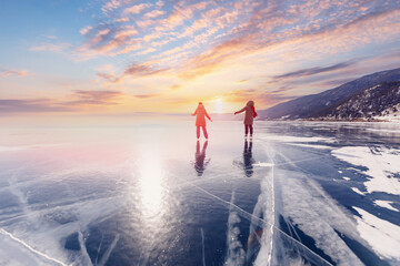 Winter lake Baikal Russia, two tourist women friends in red cap are skating on ice frozen, sunny...