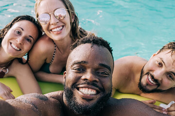 Multiracial friends at pool party having fun taking a selfie during summer vacation - Focus on african man face - Powered by Adobe