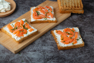 Home made bread on a wooden cutting board with curd cheese, salmon and herbs