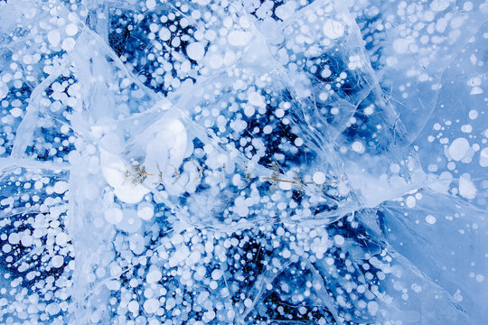 Gas methane bubbles and seaweed frozen in winter ice of lake Baikal, abstract background