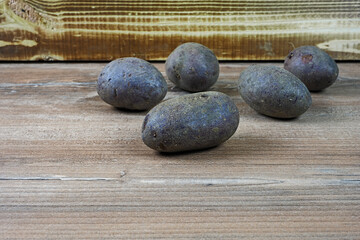 Fünf Kartoffeln der lilafarbenen Sorte Violetta auf Holz vor einer Holzkiste