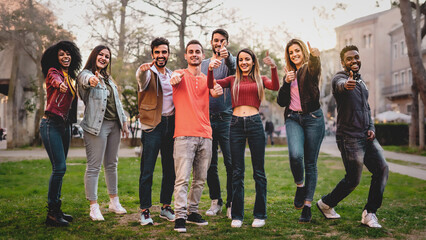 Multiethnic group of people looking at camera thumbs up - positive diverse young friends having fun...