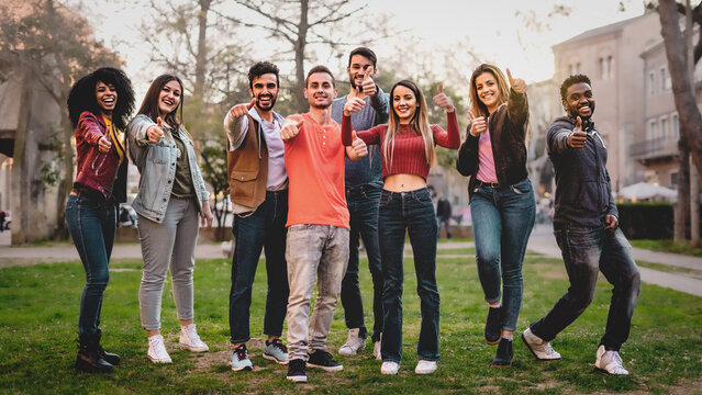 Multiethnic group of people looking at camera thumbs up - positive diverse young friends having fun in the park - concept of trust and diversity