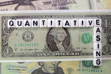 Quantitative Easing written on white cube with dollars background for QE concept.