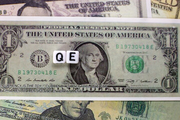 QE written on cube with dollars background for quantitative easing concept.