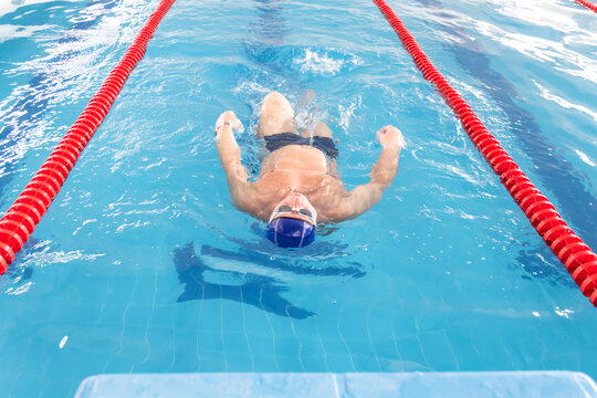 A male athlete swims in a swimming pool sports complex in blue water.