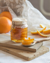 Homemade candied peels orange confiture in glass jar on light background, selective focus