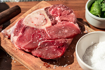 A fresh raw beef ossobuco steak on a board with garnishes on a wooden table. Animal protein concept, Italian food.