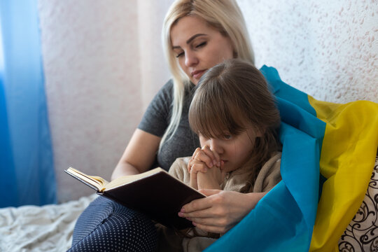 mother and daughter reading a book with the flag of ukraine in bed