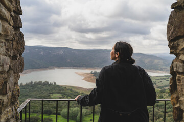 Chica joven guapa en balcón de piedra mirando zona montañosa en pueblo blanco andaluz