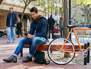 Enjoying city life. Shot of a man using his cellphone while taking a break in the city with his bicycle beside him.