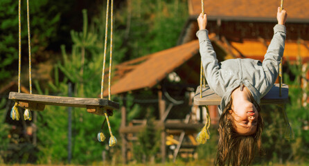 Young beautiful girl hanging upside down and having fun on a swing outdoor. Happy childhood, summer vacation, holiday and rest concept. Copy space