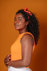 Mid waist portrait of african american woman with dark hair and orange clothes. Vertical side view of african woman with sad expression in orange background. People and color concept. - obrazy, fototapety, plakaty