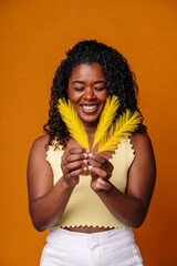 Mid waist portrait of afro woman holding yellow soft feathers. Vertical front view of native...