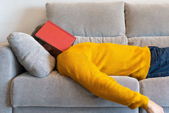 Man lying on the sofa sleeping with an open book covering his face