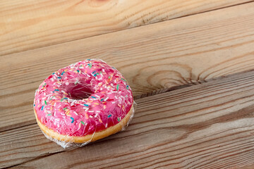 delicious pink donut in plastic packaging on an old wooden surface