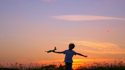 A teenage boy runs through the meadow in the rays of the setting sun. The boy has a toy plane in his hands. The boy dreams of flying on an airplane like a bird. Children's dreams of the future