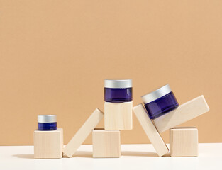 cosmetic products in a blue glass jar with a gray lid stand on a wooden podium made of cubes. Blank...
