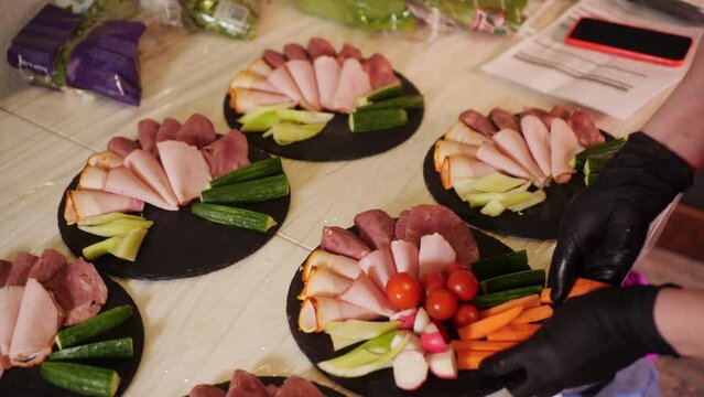 Chief Hands in Black Gloves Put Vegetables. Platter of fresh antipasto food at a party, Sliced Beef Cucumber and Parrot on Plate Top View. . High quality 4k footage