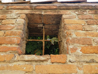 Brick wall, small old square window with iron grate.