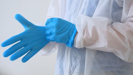 A doctor puts on gloves before working in a covid hospital with infected patients. A health worker in a protective suit puts on blue latex gloves, carefully protects exposed skin. Coronovirus concept
