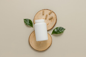 Medical vitamin bottle mockup with herbal pills and green leaves on wooden stand top view. Organic...