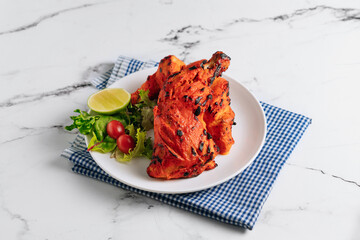 indian culture Tandoori chicken with lime in a dish isolated on napkin side view on grey background - obrazy, fototapety, plakaty