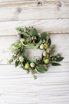 green wreath with easter quail eggs and flowers on wooden background