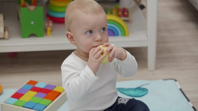 Kid eating an apple while watching tv at home, 10 month old caucasian baby boy sitting on the floor at home. High quality 4k footage