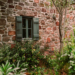 Fototapeta na wymiar A solitary window overlooks the small garden of an old stone house. Pachia Rachi, Aegina, Greece.