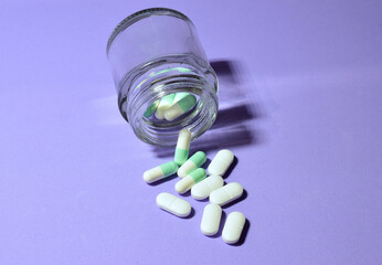 Medicines, in pills on the light mauve background and in a small glass container. 