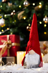 Vertical shot of a stuffed Christmas gnome on a fluffy rug under the bright glowing tree