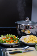 Closeup shot of boiling water in a pot and vegetables cut for salad